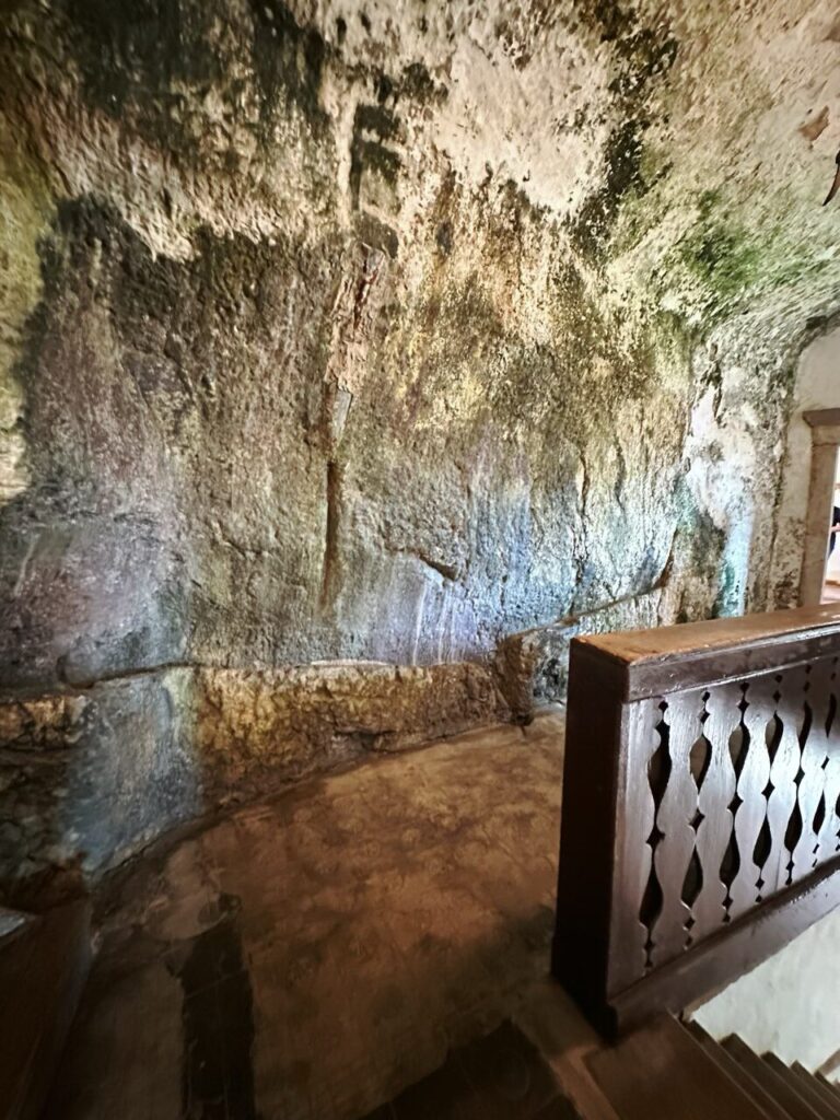 A wooden railing stands beside a rough stone wall inside Predjama Castle