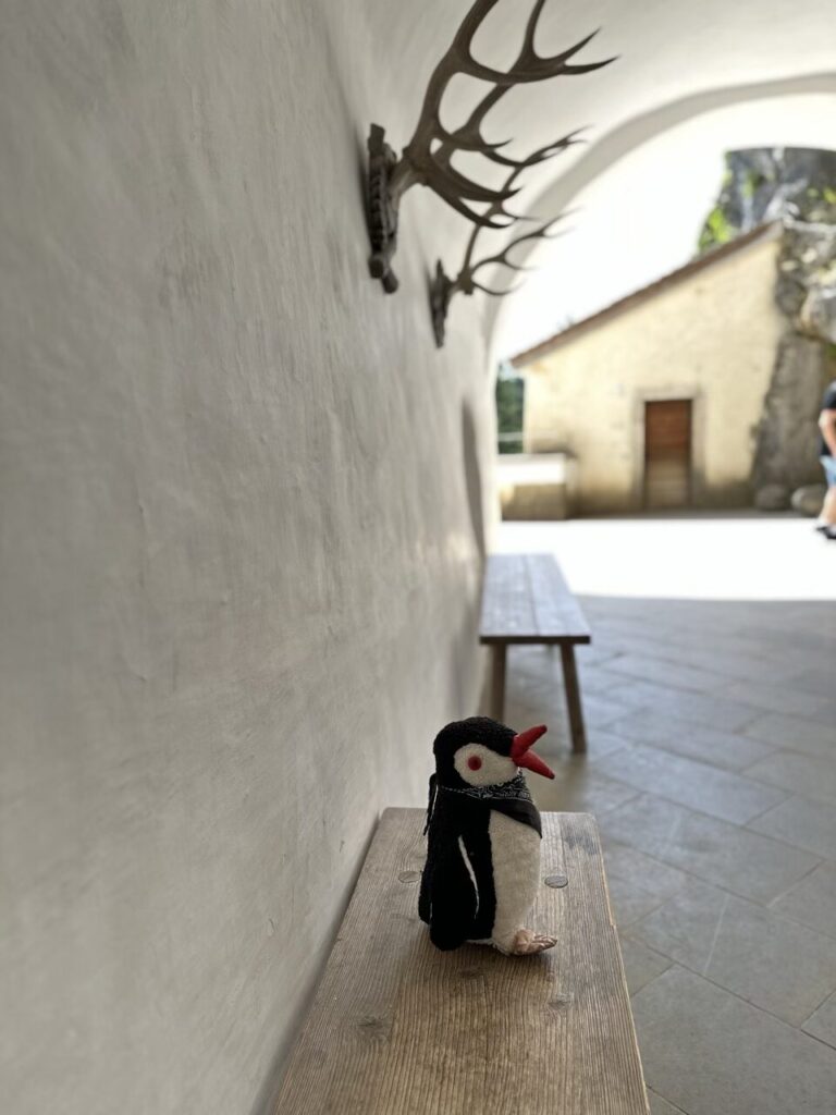 A small stuffed penguin sits on a wooden bench at Predjama Castle