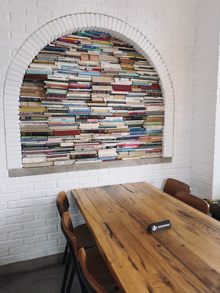 An arched wall niche filled with stacked books behind a wooden table in Slovenia
