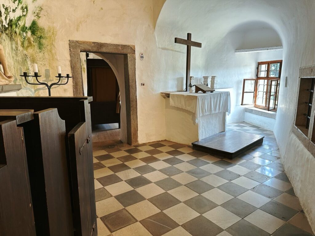 Small chapel with a wooden cross and checkered floor inside Predjama Castle