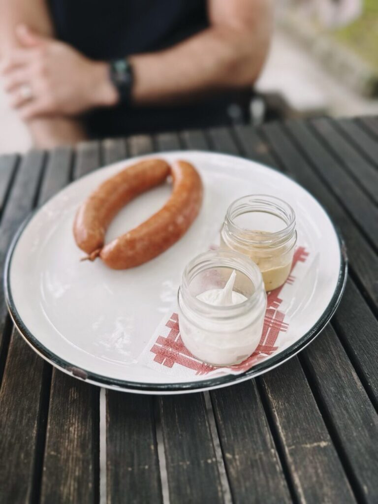 A sausage served with small jars of mustard and cream in Slovenia