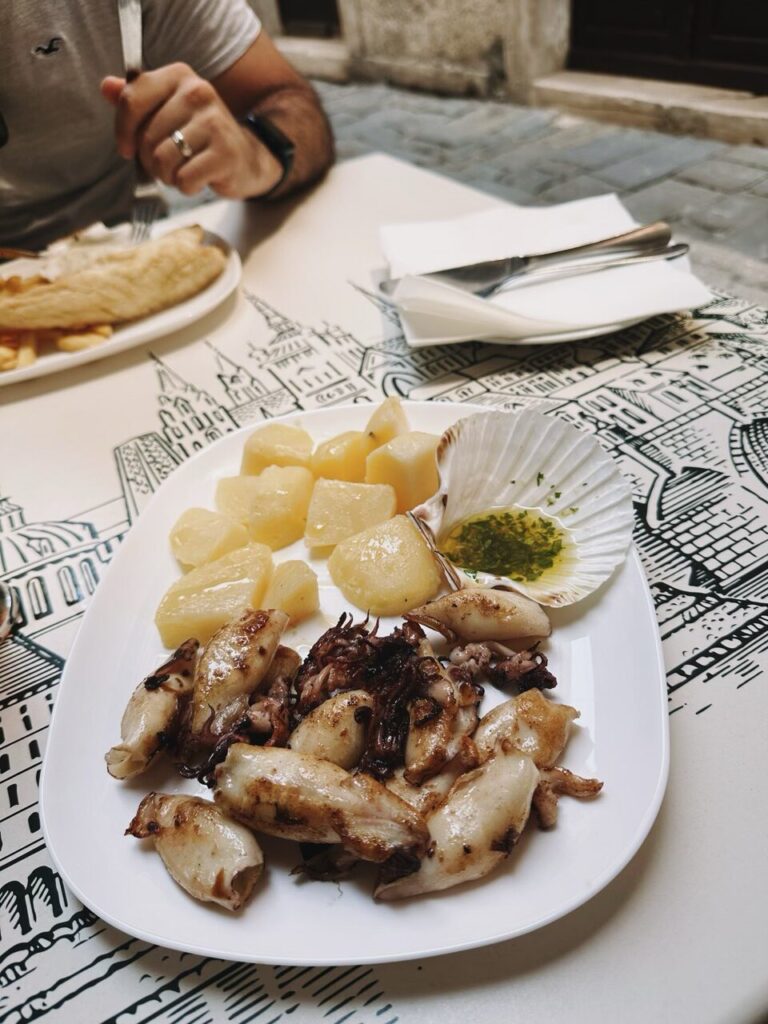 Grilled squid and potatoes served on a plate with a shell of sauce