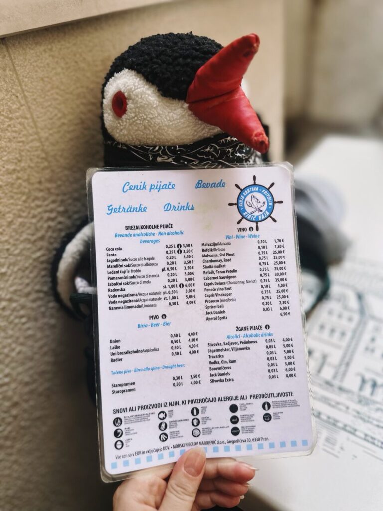 Stuffed penguin toy holding a restaurant drink menu in Piran, Slovenia