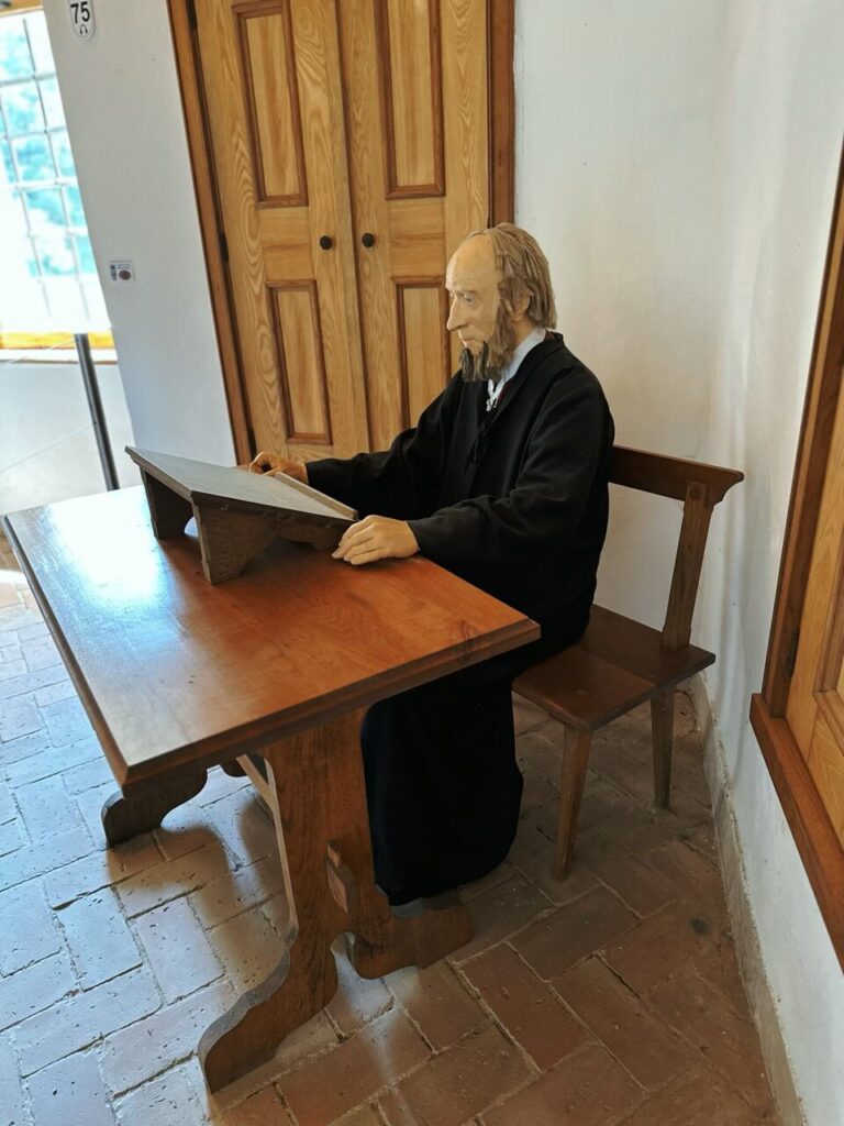 A mannequin dressed in black sits at a wooden desk inside Predjama Castle