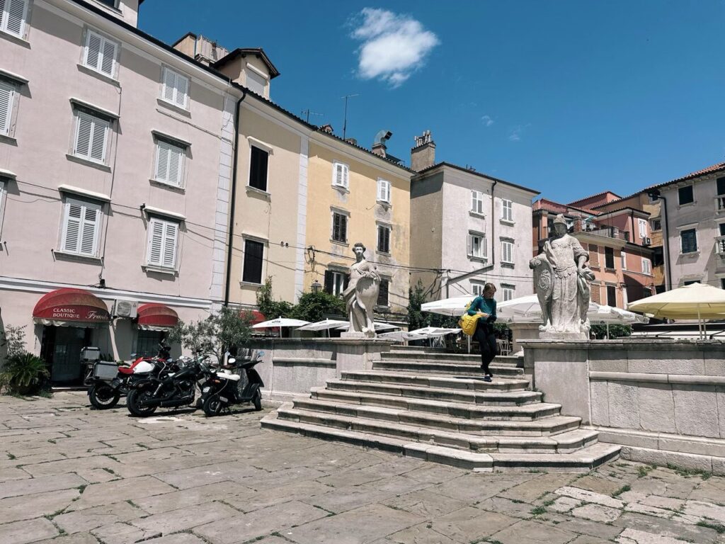 Person walking down stone steps in a sunny square in Piran