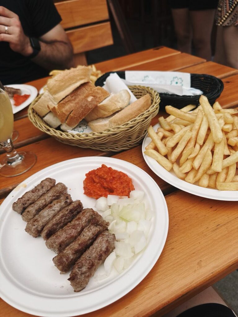 Grilled meat sausages served with onions, red pepper spread, bread, and french fries