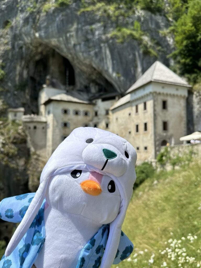 Predjama Castle with the plush penguin mascot Miško in the foreground