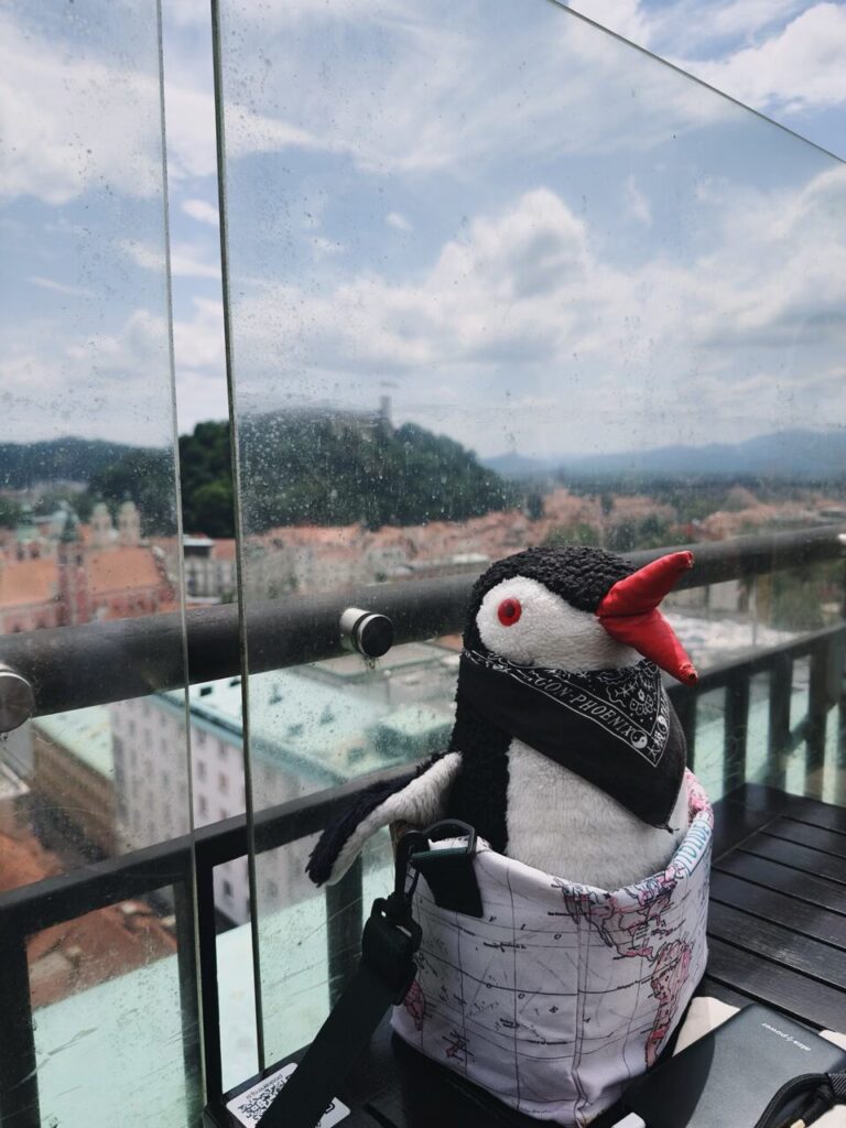 Stuffed penguin in a map bag overlooking the city of Ljubljana