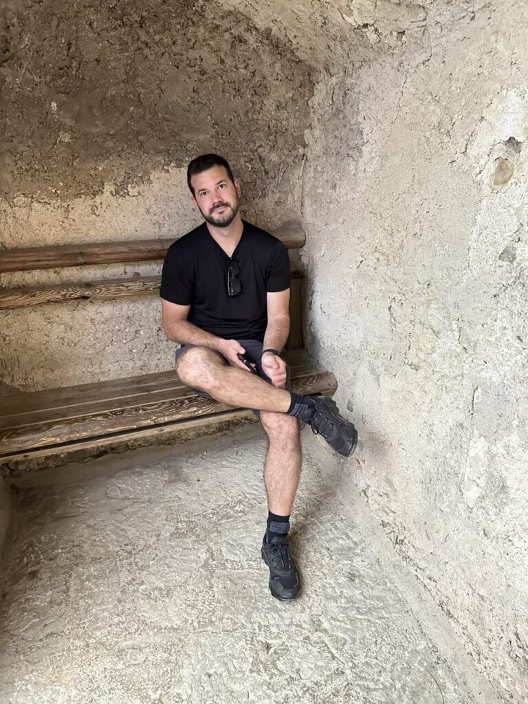 Man sitting on a wooden bench inside a stone alcove at Predjama Castle